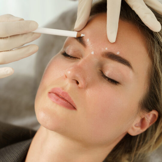 Doctor making marks on client's face before filler injections in aesthetics medical clinic