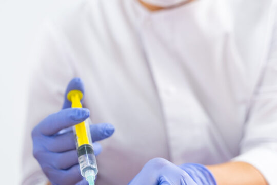 Professional young cosmetologist in sterile latex gloves administering a fat-dissolving injection into her patients abdomen